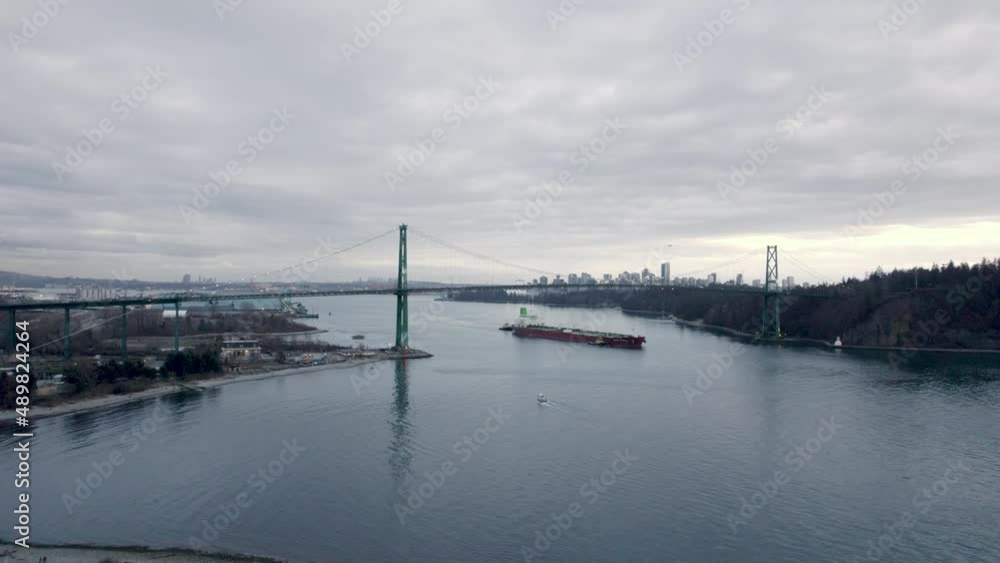 Barge passing under Lions Gate bridge with city and skyscrapers in background, Vancouver in Canada. Aerial forward Barge passing under Lions Gate bridge with city and skyscrapers in background, Vancouver in Canada. Aerial forward