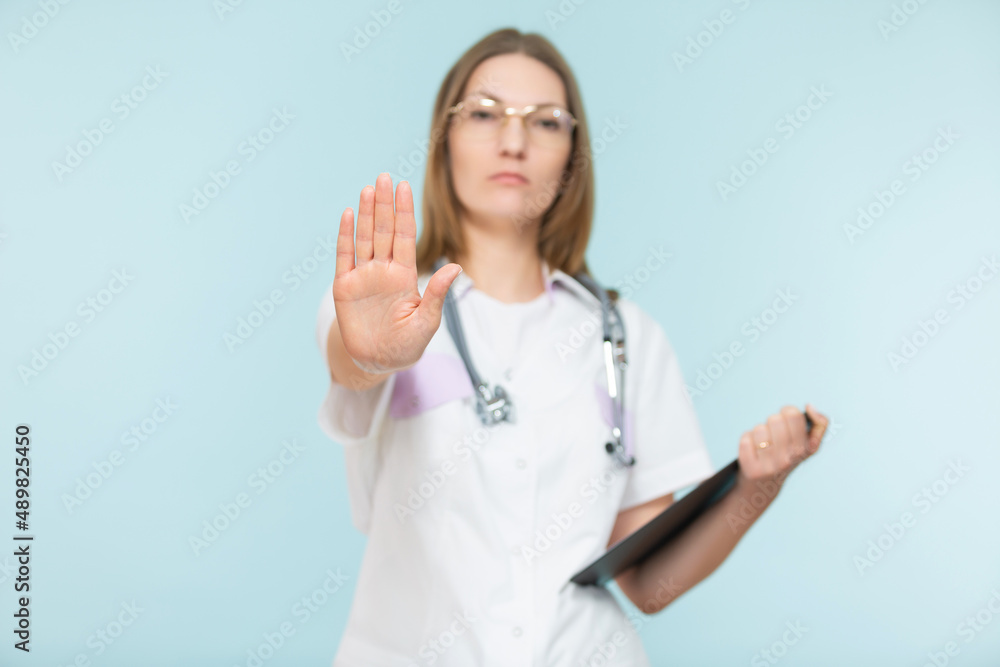 Beautiful woman doctor with a stethoscope and a black tablet, shows a stop sign with her hand, on a blue background. Copy paste. healthcare concept. Let's stop the disease. Beautiful woman doctor with a stethoscope and a black tablet, shows a stop sign with her hand, on a blue background. Copy paste. healthcare concept. Let's stop the disease.