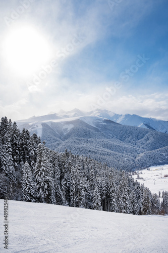 Beautiful landscape of the Arkhyz ski resort with mountains, snow, forest and track on a sunny winter day. Caucasus  Mountains, Russia. Vertical orientation © Kufotos