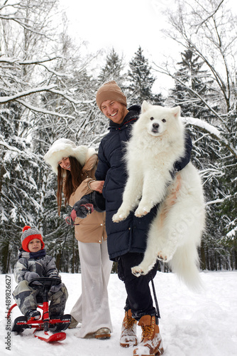 Fototapeta Naklejka Na Ścianę i Meble -  Family of mother, father and son having fun in snowy winter wood with cheerfull pet dog.