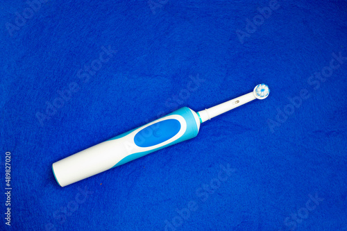 Modern electric toothbrush standing on a blue background. Controlled tool for daily oral care