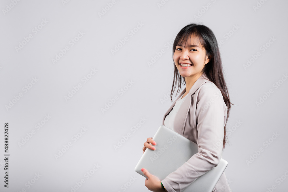 Side view woman smiling confident smiling holding closed laptop, Portrait excited happy Asian young female person hugging close cover computer device studio shot isolated on white background Side view woman smiling confident smiling holding closed laptop, Portrait excited happy Asian young female person hugging close cover computer device studio shot isolated on white background