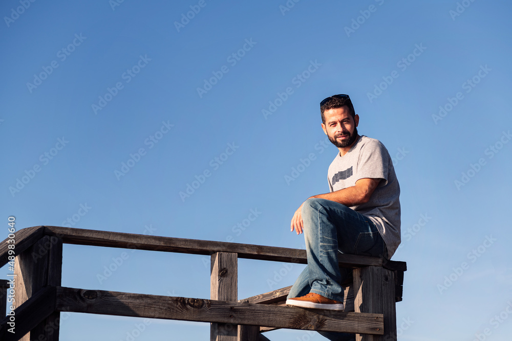 Fototapeta premium man looking at camera sitting on a wooden railing