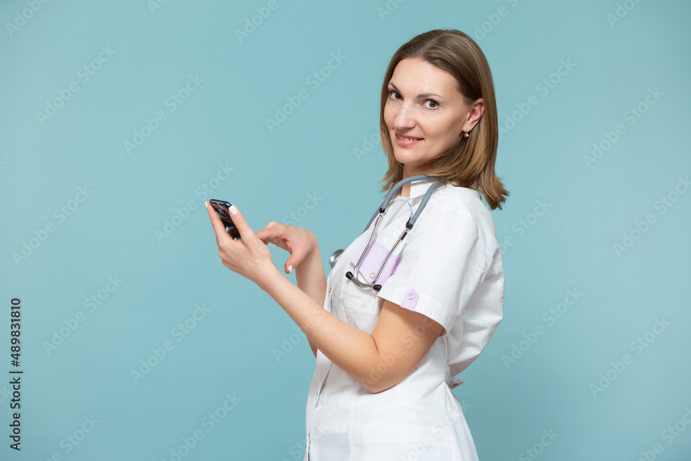 A woman doctor with a smartphone conducts an online consultation, supports the patient by phone, on a blue background. Copy paste. Distance healthcare concept. A woman doctor with a smartphone conducts an online consultation, supports the patient by phone, on a blue background. Copy paste. Distance healthcare concept.