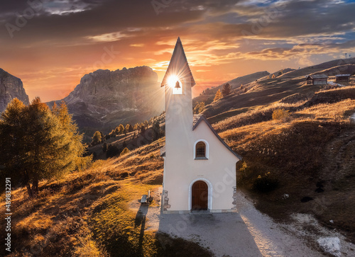 South Tyrol, Italy - The setting sun is shinning through the Chapel of San Maurizio (Cappella Di San Maurizio) at the Passo Gardena Pass in the Italian Dolomites at autumn with warm sunlight photo
