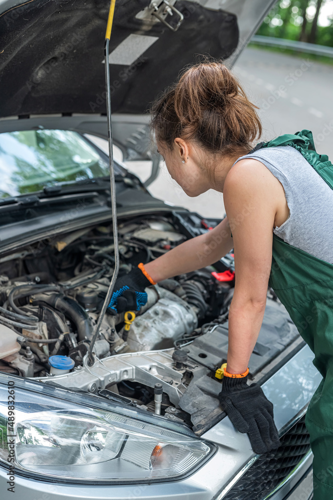 female mechanic wear green uniform checking level of oil on a car engine dipstick female mechanic wear green uniform checking level of oil on a car engine dipstick