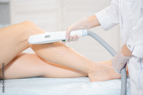 Closeup of the patient legs lying in the beauty salon and the beautician hands performing the laser hair removal procedure with modern instruments