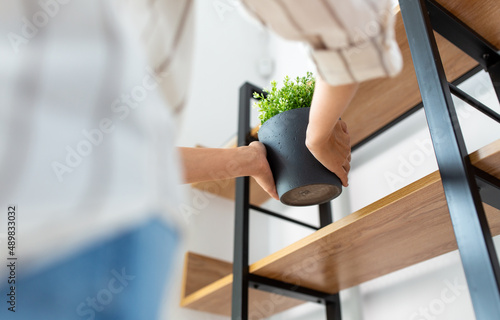 home improvement, decoration and people concept - close up of woman with flower or houseplant at shelf