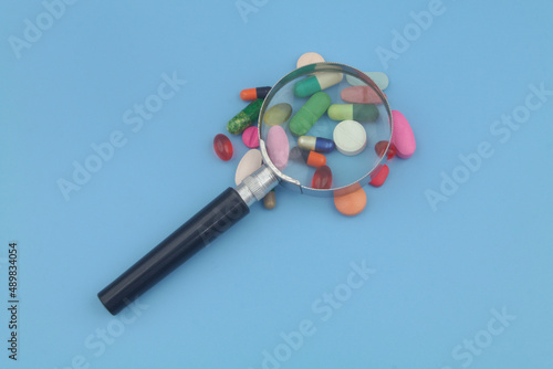 Drugs with magnifying glass on blue background. Review drugs concept.