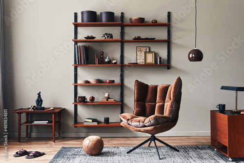 Stylish interior of living room with design brown armchair, wooden bookcase, pendant lamp, carpet decor, picture frames and elegant personal accessories in modern retro home decor. Template. © FollowTheFlow