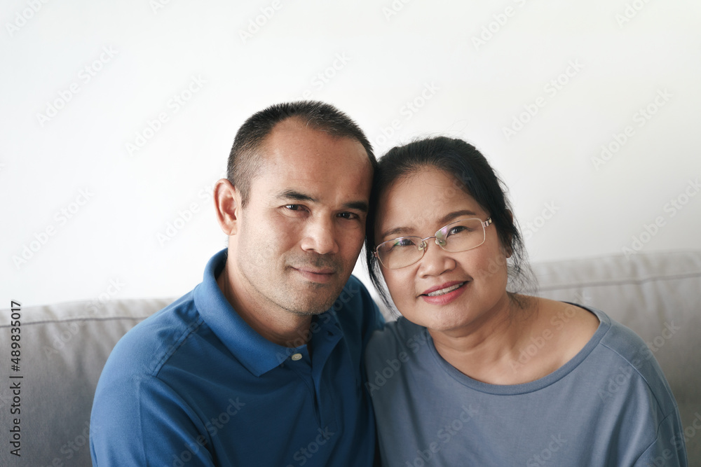 Portrait of Asian mature couple sitting in the living room. wife and husband hugging, holding hand with happiness and cheerful. Love, safety, and insurance family concept. Portrait of Asian mature couple sitting in the living room. wife and husband hugging, holding hand with happiness and cheerful. Love, safety, and insurance family concept.