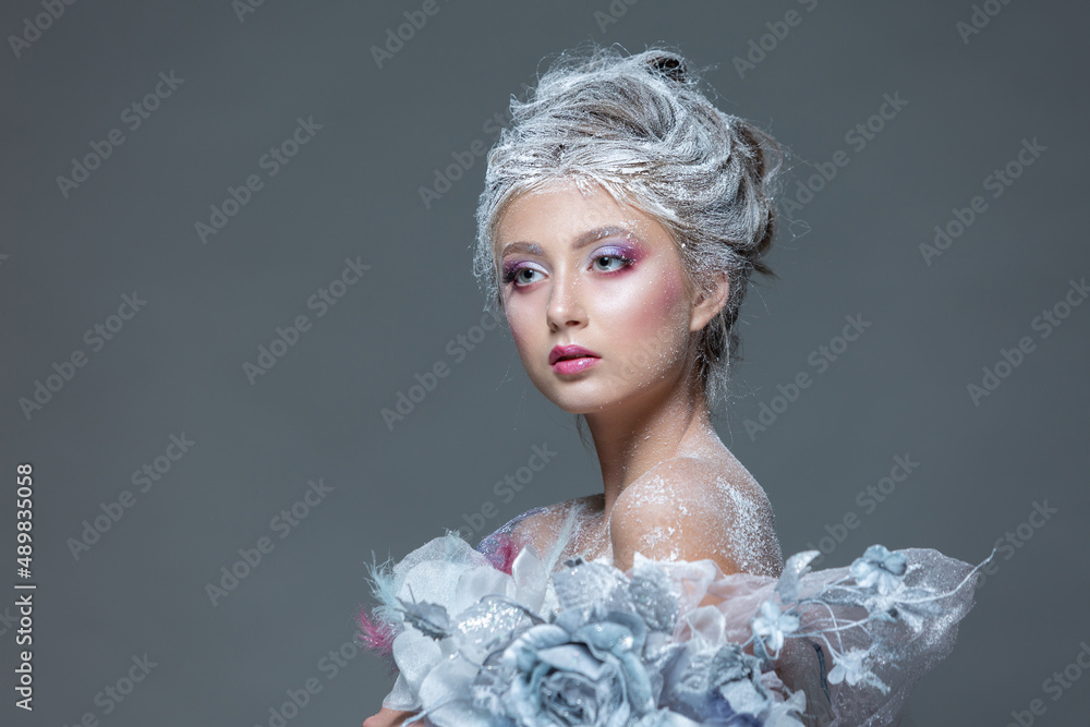 Winter Beauty Woman in clothes made of frozen flowers covered with frost, with snow on her face and shoulders. Christmas Girl Makeup. Make-up the snow Queen. Isolated on a gray background.