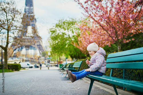 Canvas Print Adorable three year old girl sitting on the bench near the Eiffel tower in Paris