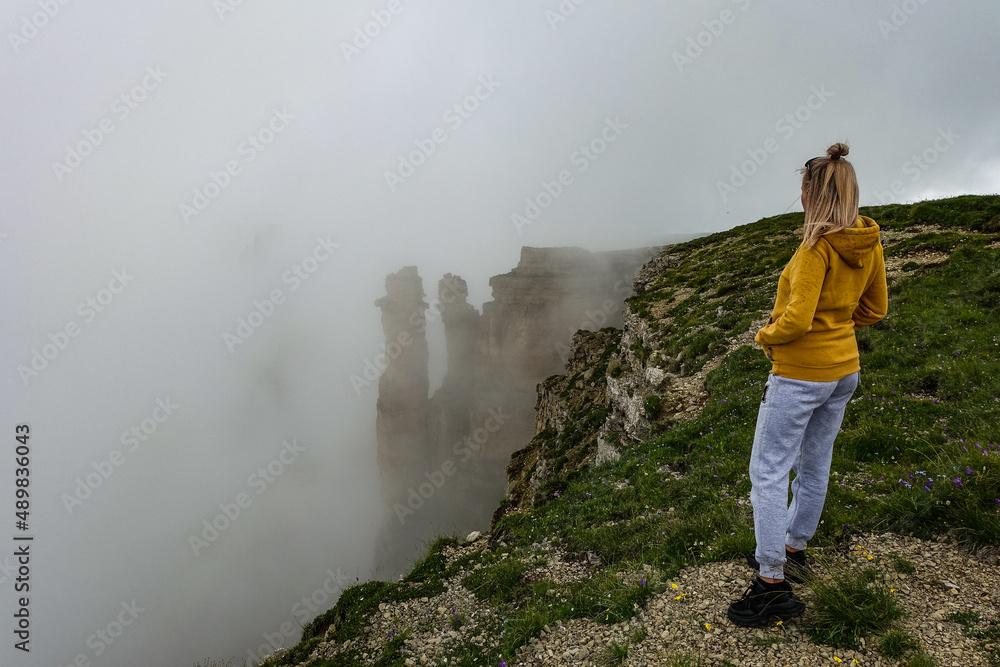 A girl against the background of two monks rocks in a cloud, Bermamyt plateau, Russia 2021. June