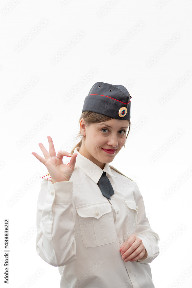 Beautiful young female Russian police officer in dress uniform shows hand signs perfectly and smiles on a white background. Selective focus. Portrait Beautiful young female Russian police officer in dress uniform shows hand signs perfectly and smiles on a white background. Selective focus. Portrait