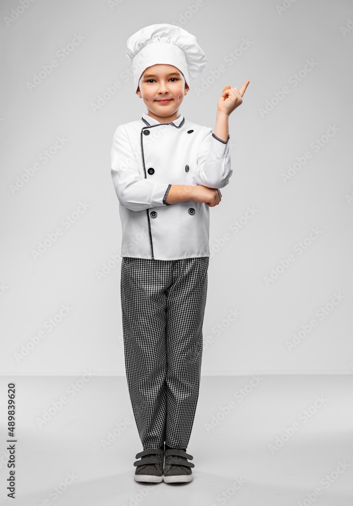 cooking, culinary and profession concept - happy smiling little boy in chef's toque and jacket pointing finger up over grey background cooking, culinary and profession concept - happy smiling little boy in chef's toque and jacket pointing finger up over grey background