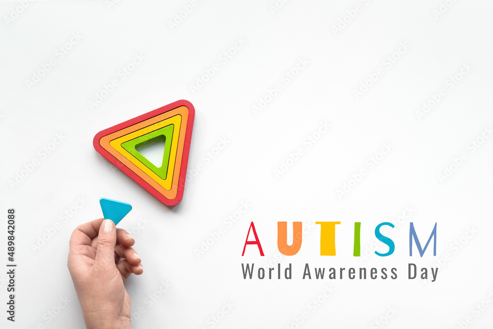 Text Autism awareness month. Nested wood triangles in rainbow colors. Concentric educational stacking puzzle. Montessori nesting sensory toy for toddlers, kids. Flat lay, top view on white paper. Text Autism awareness month. Nested wood triangles in rainbow colors. Concentric educational stacking puzzle. Montessori nesting sensory toy for toddlers, kids. Flat lay, top view on white paper.