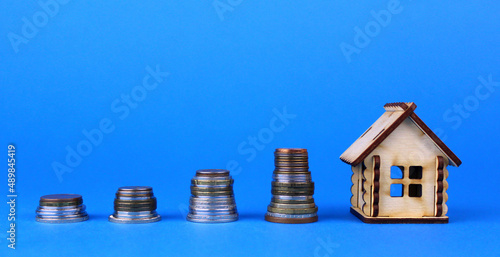 Small wooden house and coins on a blue background. The concept of accumulating money and rising real estate prices
