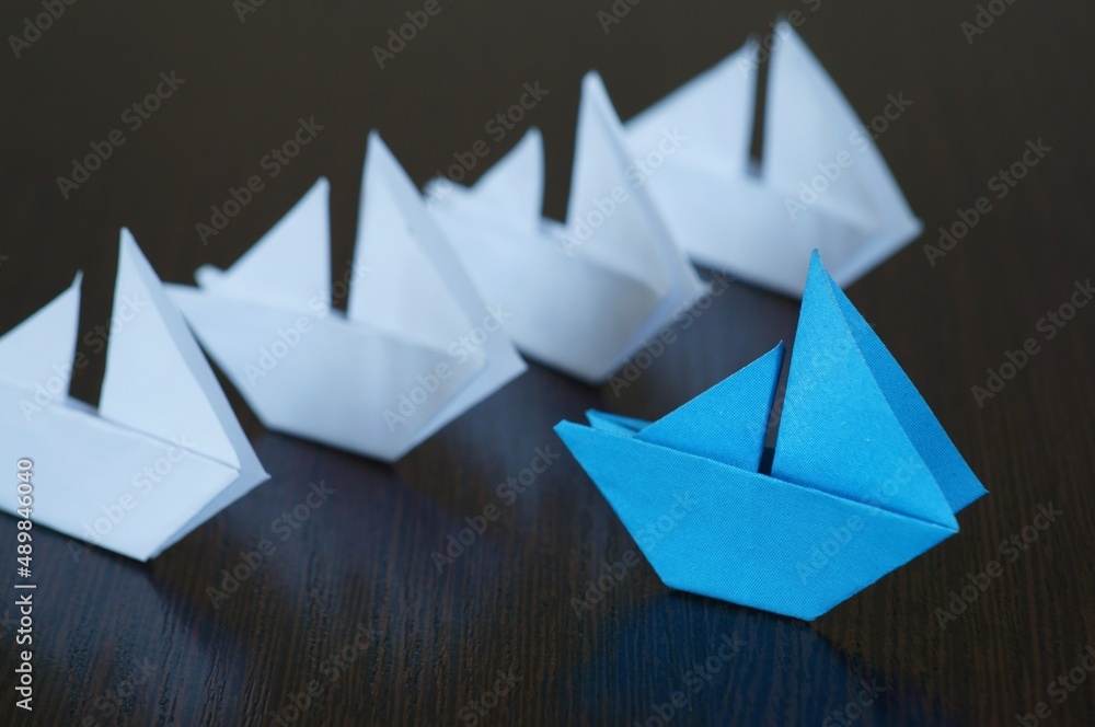 Several white paper boats and a blue one on the table. Several white paper boats and a blue one on the table.