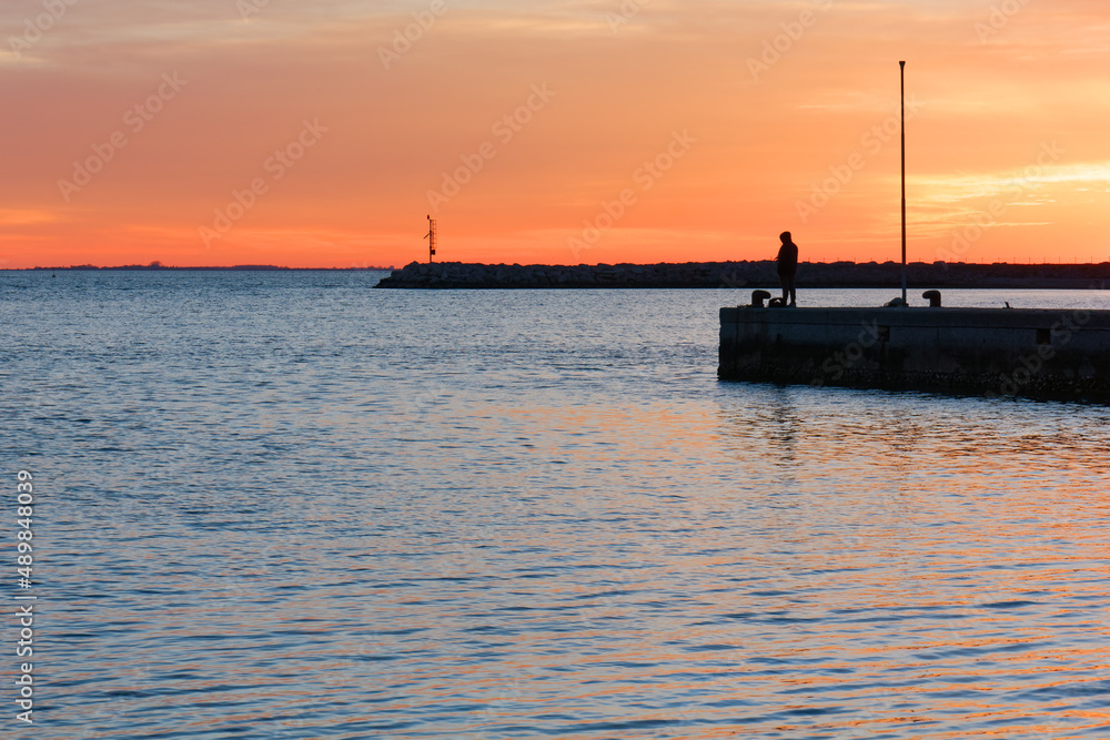 Man fishing during a winter sunset on a pier at Sistiana bay near Trieste, Italy