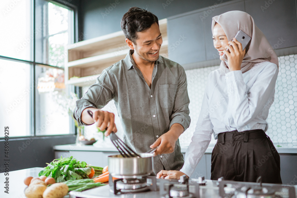 muslim couple cooking their food in the kitchen while wife taking a phone call muslim couple cooking their food in the kitchen while wife taking a phone call