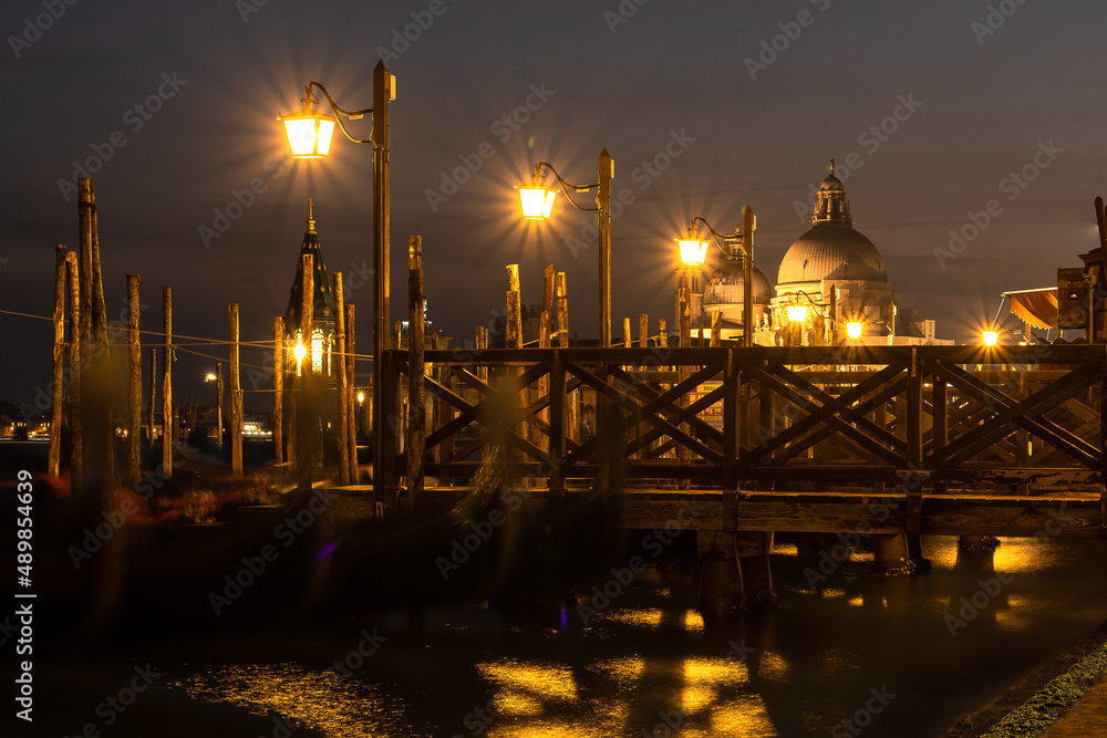 Venice, Italy: November 24 2021. Small pier in Venice at night, with gondolas and the Basilica of Santa Maria della Salud in the background