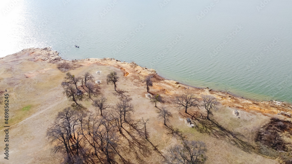 Fototapeta premium Small boat fishing near curved rocky shoreline with drop-offs, cliffs and bluffs at at Grapevine Lake, Texas, America