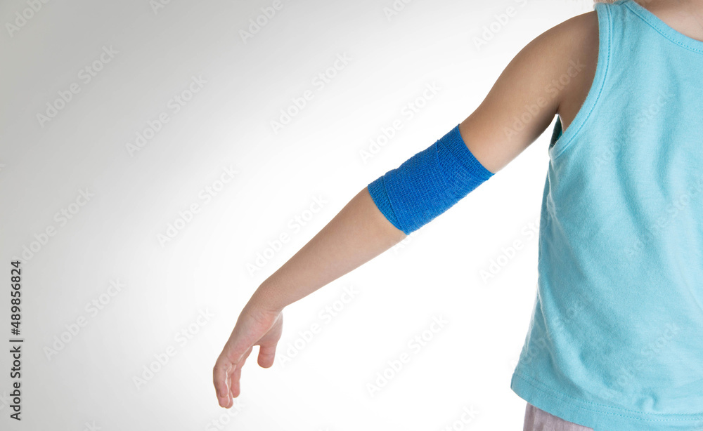 Blue elastic bandage on the elbow joint of the child on the arm. White background, close-up. Hand pain Blue elastic bandage on the elbow joint of the child on the arm. White background, close-up. Hand pain