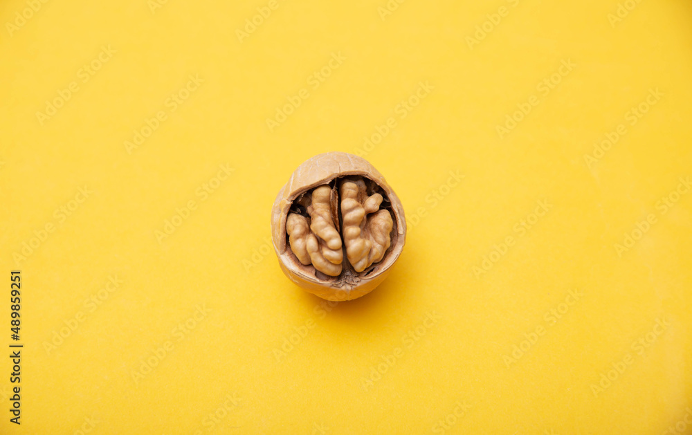 Walnut with broken shells on a yellow background, close-up. Walnut resembling a human brain Walnut with broken shells on a yellow background, close-up. Walnut resembling a human brain