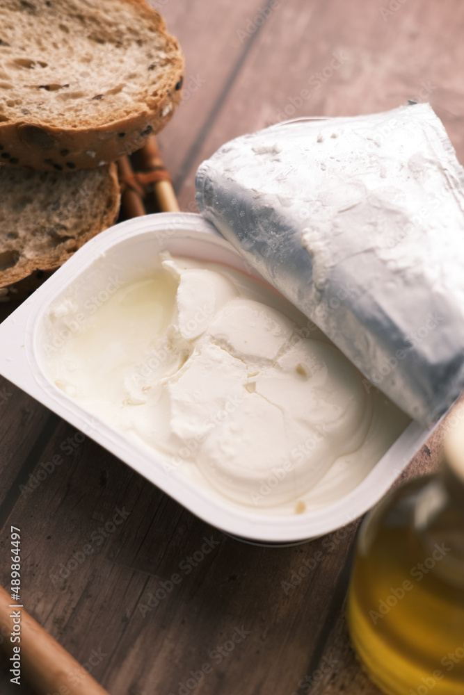 cheese cream in a container with bread and oil on table 