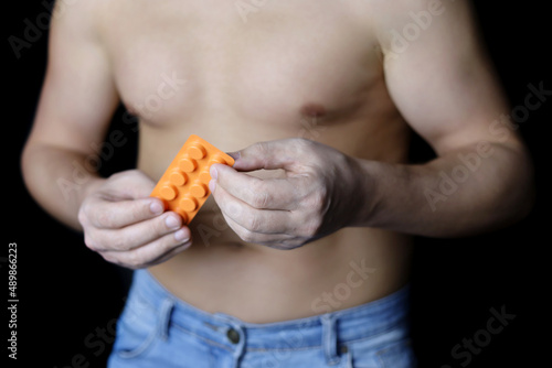 Muscular man with naked torso taking pills, pack with tablets in male hands close up. Concept of medication for stomach, vitamins, sleeping or digestive pill