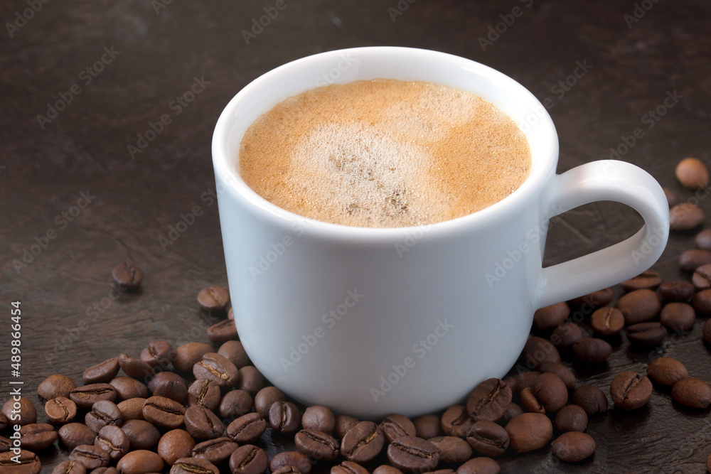 white cup of coffee with coffee beans on a dark background. close-up white cup of coffee with coffee beans on a dark background. close-up