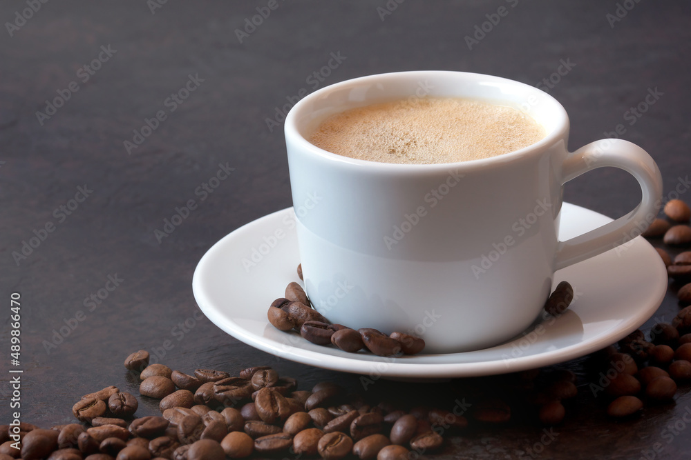 white cup of coffee on a saucer with coffee beans on a dark background. front view white cup of coffee on a saucer with coffee beans on a dark background. front view
