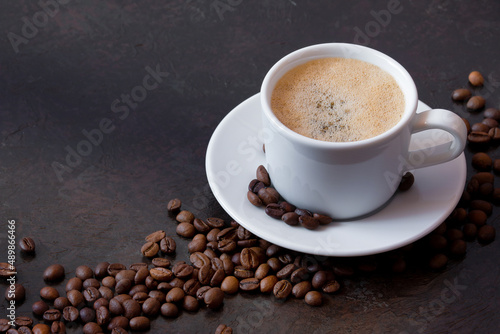 white cup of coffee on a saucer with coffee beans on a dark background