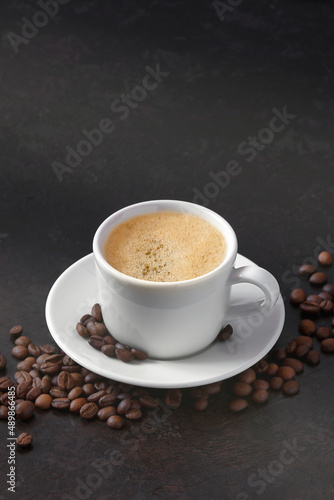 white cup of coffee on a saucer with coffee beans on a dark background. vertical image