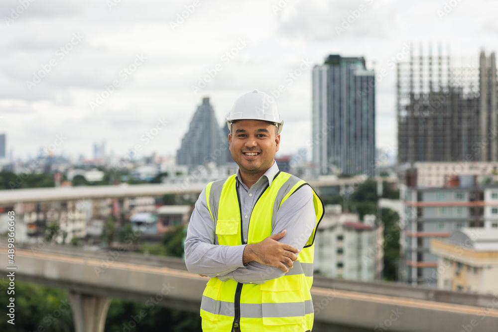 Asian engineer man or architect looking forward with white safety helmet in city construction site . Standing on rooftop building construction at capital. Asian engineer man or architect looking forward with white safety helmet in city construction site . Standing on rooftop building construction at capital.