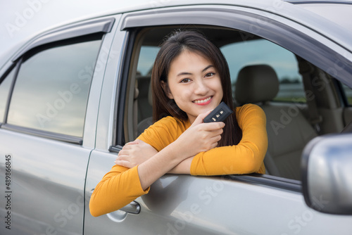 Young beautiful asian women getting new car. she very happy and excited looking outside window in hand holding car key. Smiling female driving vehicle on the road on a bright day © Chanakon