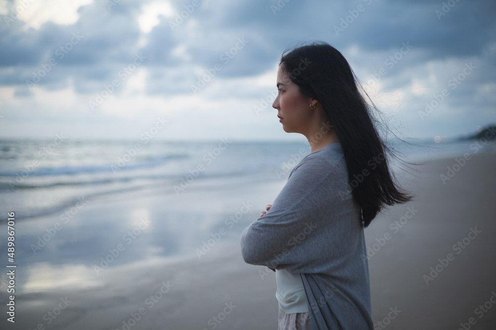 A sad and stressed Asian woman stands alone on the beach in the evening. Dramatic atmosphere. disappointment in life. She stood crying alone A sad and stressed Asian woman stands alone on the beach in the evening. Dramatic atmosphere. disappointment in life. She stood crying alone
