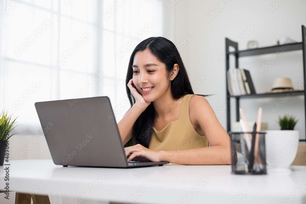 Young asian beautiful business woman working with laptop sitting at home. Smiling charming happy young female doing homework meeting conference with team at home. Young asian beautiful business woman working with laptop sitting at home. Smiling charming happy young female doing homework meeting conference with team at home.