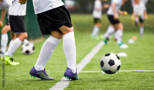 Soccer Player With White and Black Football Ball. Young Athlete Kicking Ball on Grass Field. Boy in White Soccer Jersey Uniform Kicking Ball. Soccer Training For Kids