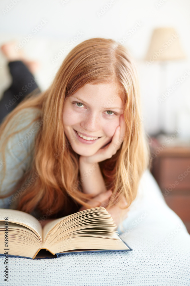 Enjoying the world of fiction. Portrait of a young redhead reading her book and lying on her bed. Enjoying the world of fiction. Portrait of a young redhead reading her book and lying on her bed.