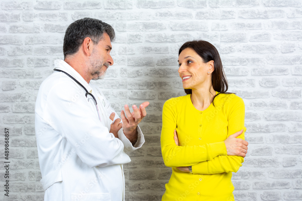 Mature male doctor consulting female patient filling form at consultation. Professional physician wearing white coat talking to woman signing medical paper at appointment visit in clinic. Mature male doctor consulting female patient filling form at consultation. Professional physician wearing white coat talking to woman signing medical paper at appointment visit in clinic.