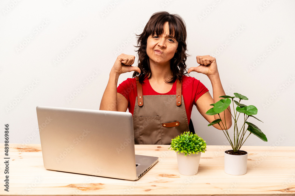 Young gardener hispanic woman sitting on a table isolated on white background feels proud and self confident, example to follow. Young gardener hispanic woman sitting on a table isolated on white background feels proud and self confident, example to follow.
