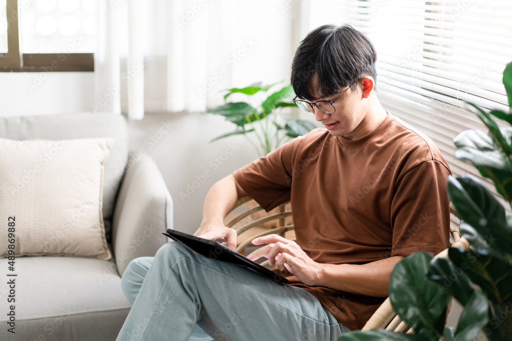 Technology Concept The male with his casual T-shirt and jeans sitting comfortably on the wooden chair and doing touchscreen for checking the web browser on the iPad