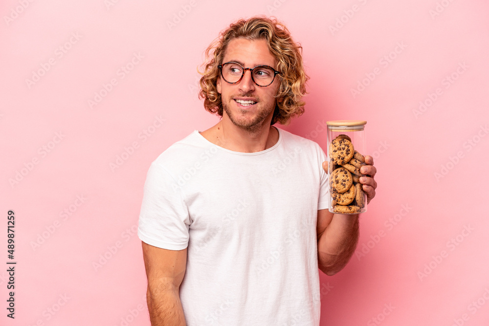 Young caucasian man holding cookies jar isolated on pink background looks aside smiling, cheerful and pleasant. Young caucasian man holding cookies jar isolated on pink background looks aside smiling, cheerful and pleasant.