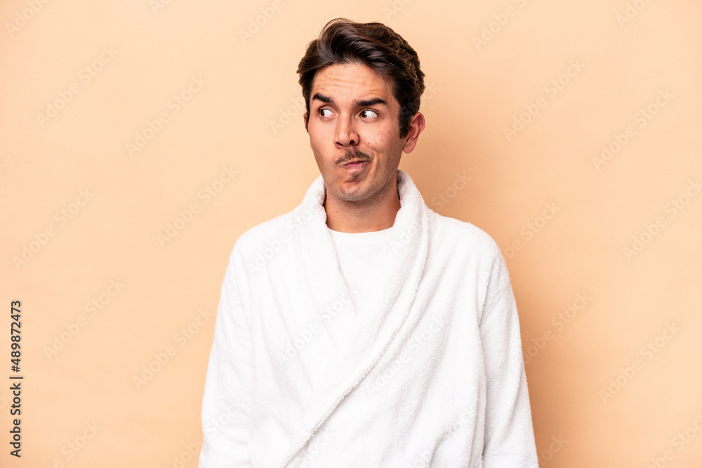 Young caucasian man wearing a bathrobe isolated on beige background confused, feels doubtful and unsure. Young caucasian man wearing a bathrobe isolated on beige background confused, feels doubtful and unsure.