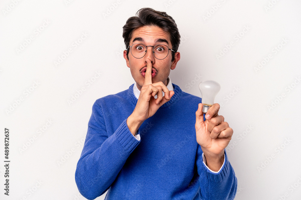 Young caucasian man holding a lightbulb isolated on white background keeping a secret or asking for silence. Young caucasian man holding a lightbulb isolated on white background keeping a secret or asking for silence.