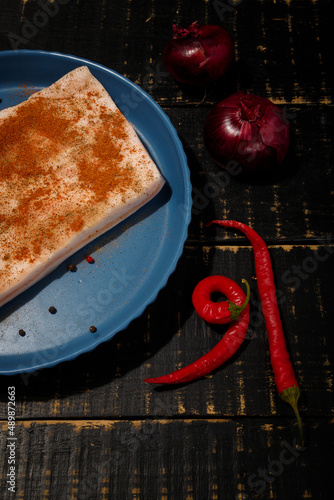 Piece of prickled pork lard with spices and flavourings. Ukrainian traditional meal on blue plate, black wooden table. Vertical shot. photo