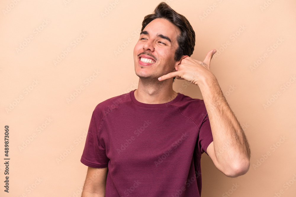Young caucasian man isolated on beige background showing a mobile phone call gesture with fingers. Young caucasian man isolated on beige background showing a mobile phone call gesture with fingers.