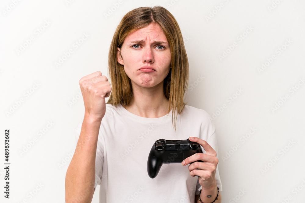 Young English woman playing with a video game controller isolated white background showing fist to camera, aggressive facial expression. Young English woman playing with a video game controller isolated white background showing fist to camera, aggressive facial expression.